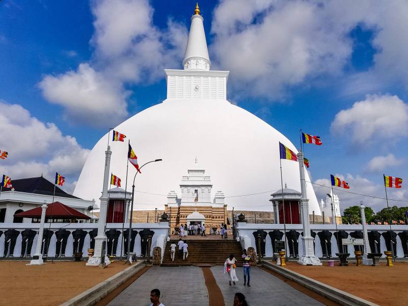 White dome of Ruwanwelisaya stupa under a blue sky with Buddhist flags, Anuradhapura, Sri Lanka