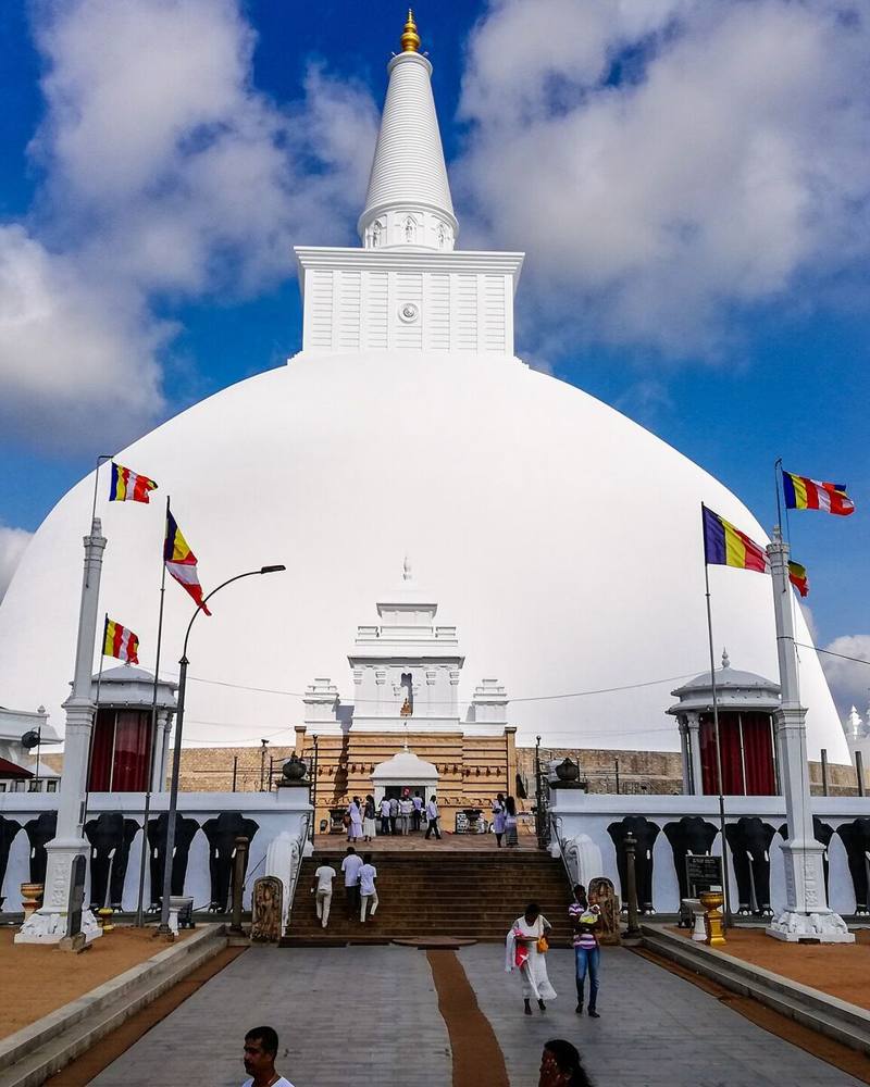 White dome of Ruwanwelisaya stupa under a blue sky with Buddhist flags, Anuradhapura, Sri Lanka