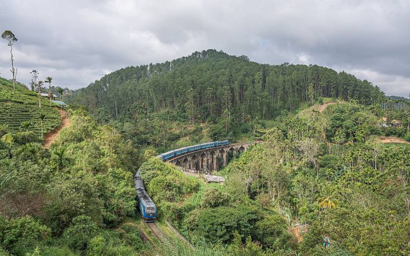 Blue train crossing the Nine Arch Bridge among forested hills and tea, near Ella, Sri Lanka