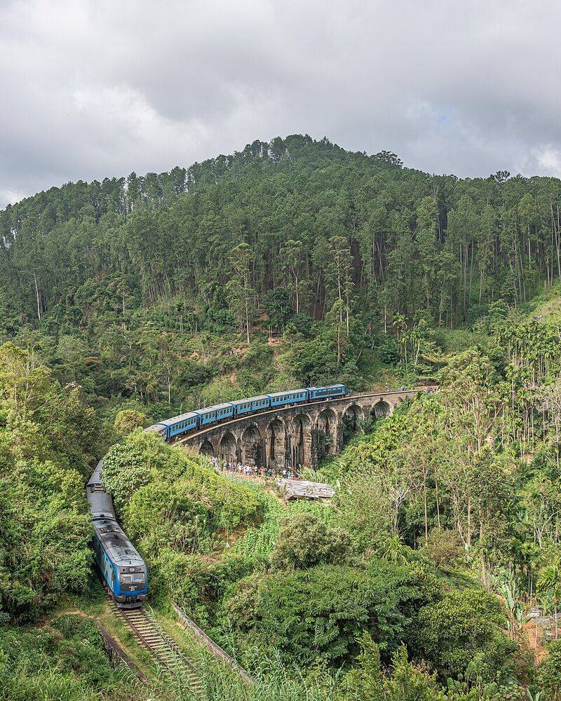Blue train crossing the Nine Arch Bridge among forested hills and tea, near Ella, Sri Lanka