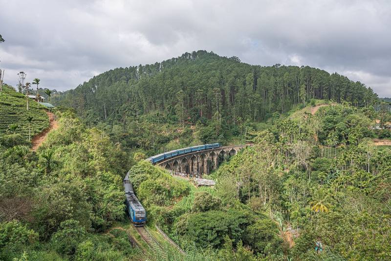 Blue train crossing the Nine Arch Bridge among forested hills and tea, near Ella, Sri Lanka