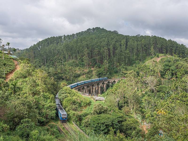 Blue train crossing the Nine Arch Bridge among forested hills and tea, near Ella, Sri Lanka