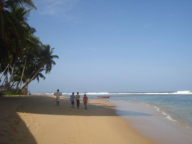 People strolling along a palm-shaded beach beside the surf, Hikkaduwa, Sri Lanka