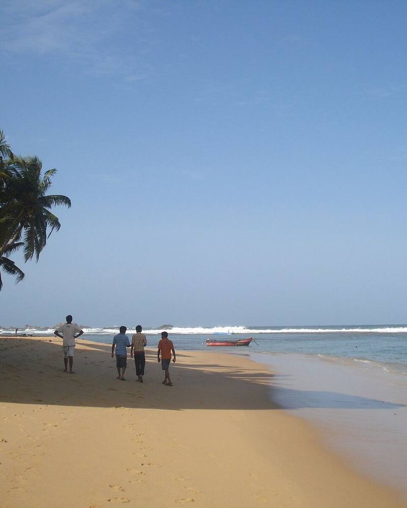 People strolling along a palm-shaded beach beside the surf, Hikkaduwa, Sri Lanka