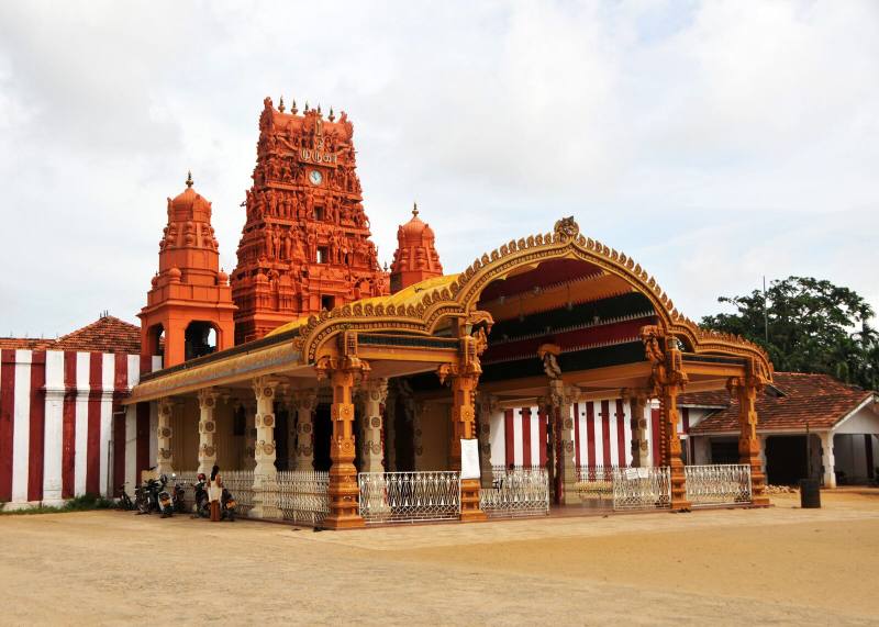 Ornate golden entrance arch and red gopuram tower of Nallur Kandaswamy Kovil beside its red and white striped walls, Jaffna, Sri Lanka