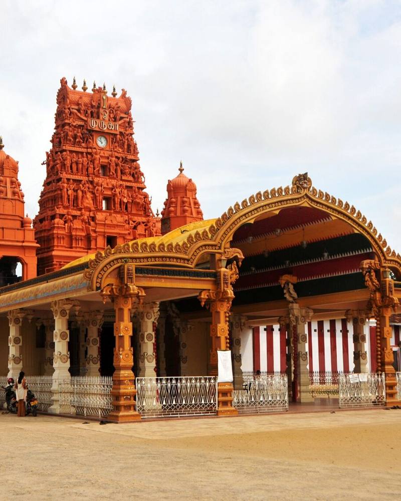 Ornate golden entrance arch and red gopuram tower of Nallur Kandaswamy Kovil beside its red and white striped walls, Jaffna, Sri Lanka