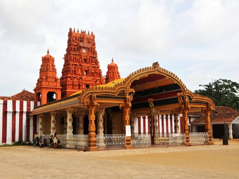 Ornate golden entrance arch and red gopuram tower of Nallur Kandaswamy Kovil beside its red and white striped walls, Jaffna, Sri Lanka