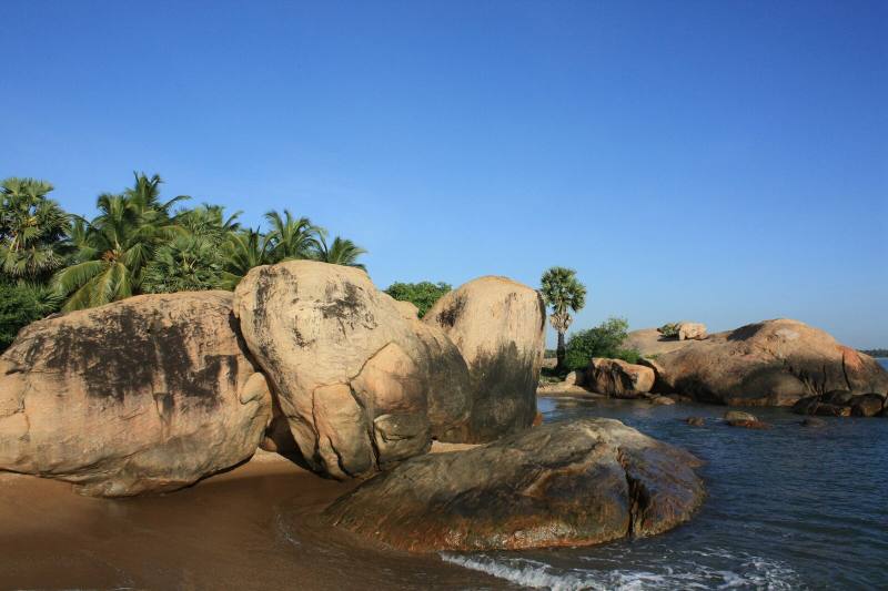 Large rounded boulders and palm trees beside calm blue water, Pasikuda, Sri Lanka